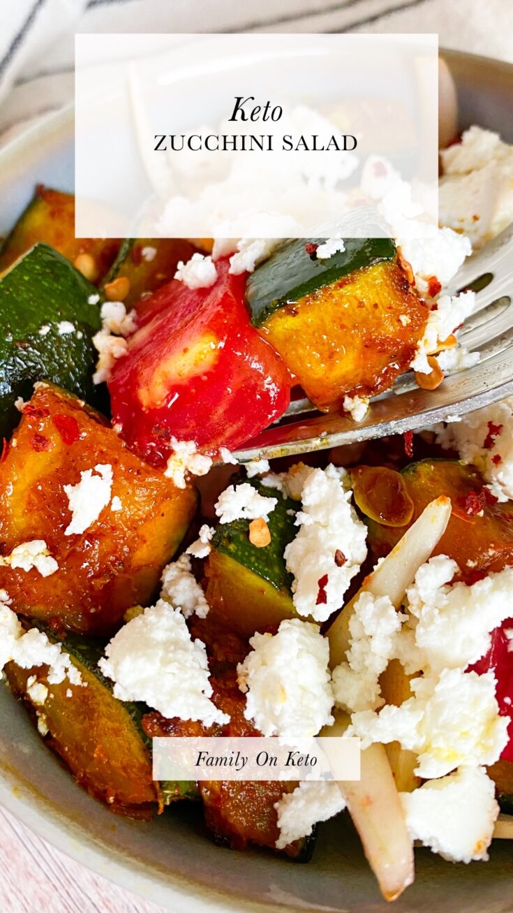 Picture of a bowl of keto zucchini salad with tomatoes, onion and feta cheese on top with zucchini and tomato cube on a fork.